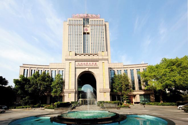 A large building with a central entrance, surrounded by a fountain and greenery.