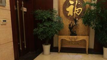 Una zona de recepción con una puerta de madera, una planta en maceta y una consola decorativa con un emblema dorado.