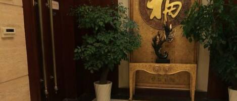 Un espace d’accueil avec une porte en bois, une plante en pot et une console décorative ornée d’un emblème doré.