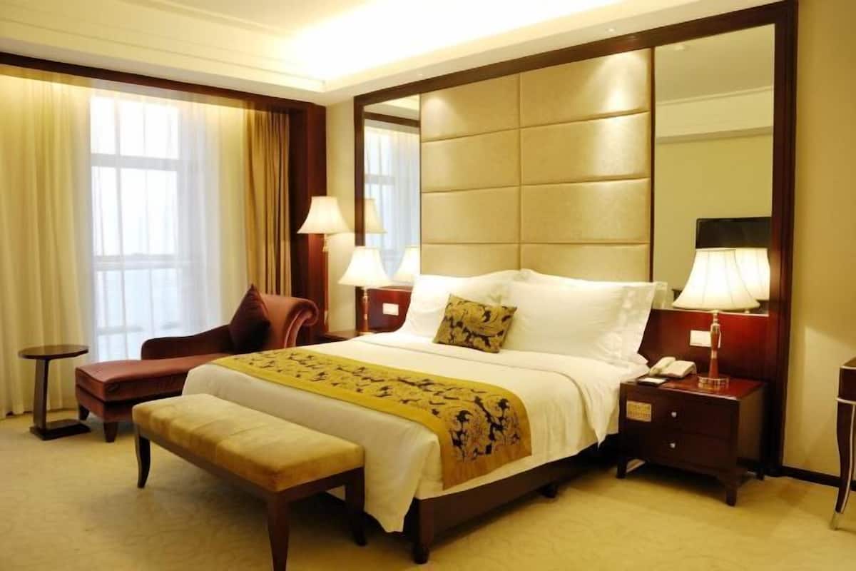 Une chambre d’hôtel avec un grand lit, une table de chevet, une chaise, une petite table et un grand miroir.