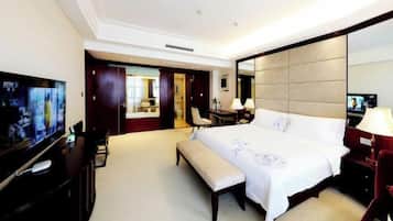 A hotel room with a large bed, a television, a desk with a lamp, and a bench.