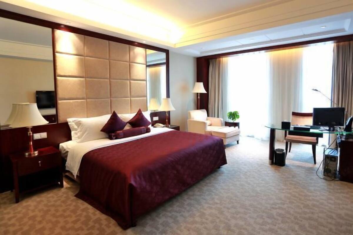 Une chambre d’hôtel avec un grand lit, un bureau, une chaise, une télévision et une fenêtre avec des rideaux.