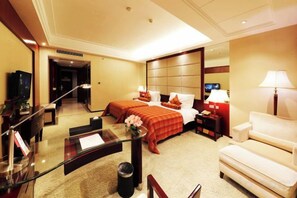 Una habitación de hotel con cama, escritorio, silla, televisor y lámpara.