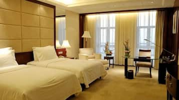 A hotel room with two beds, a desk, a chair, a lamp, and a window with curtains.