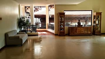 A spacious living room with a sofa, a wooden cabinet, and a large window overlooking a balcony with a tiled roof.