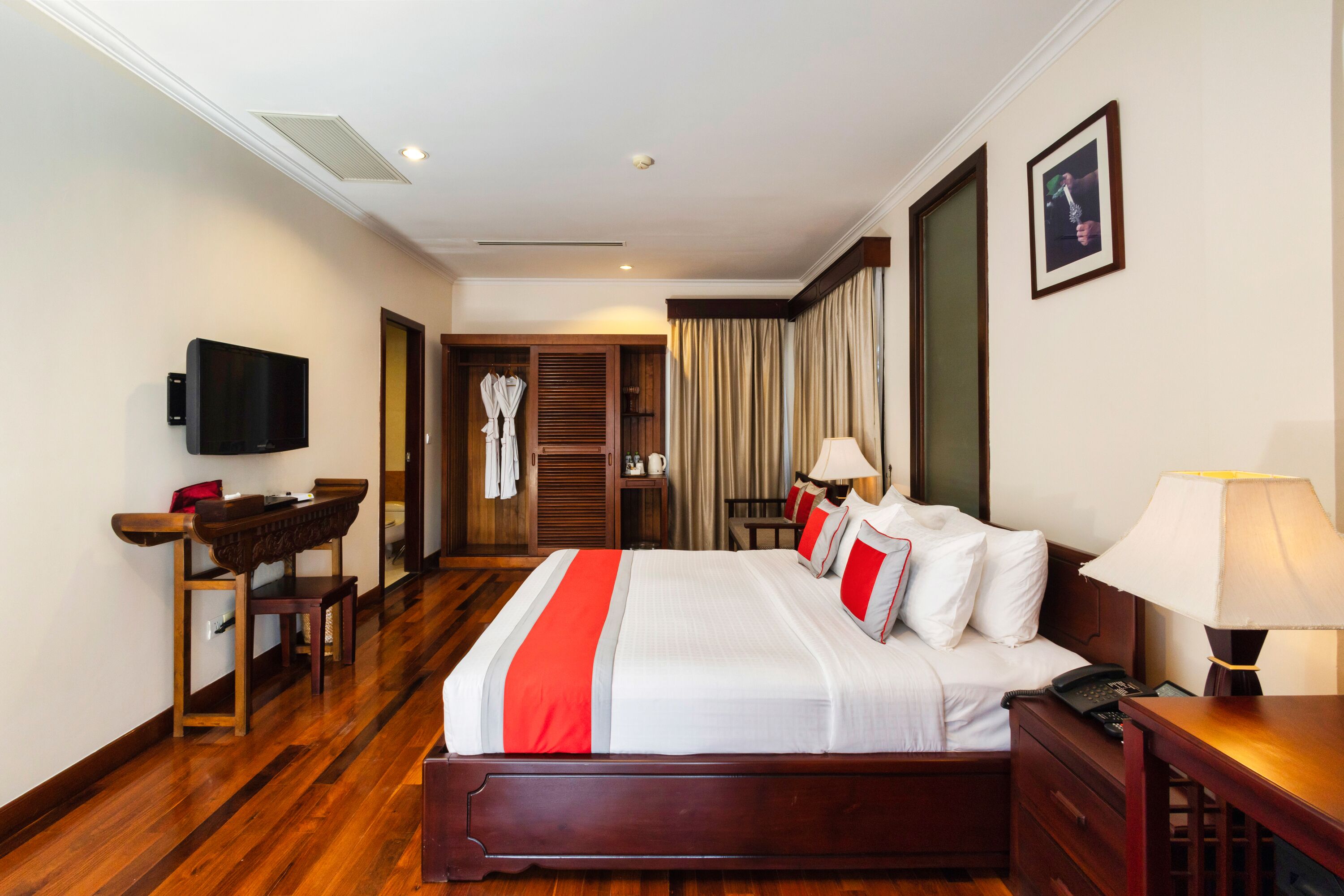 A hotel room with a large bed, bedside tables, a TV, a desk, and a wardrobe.