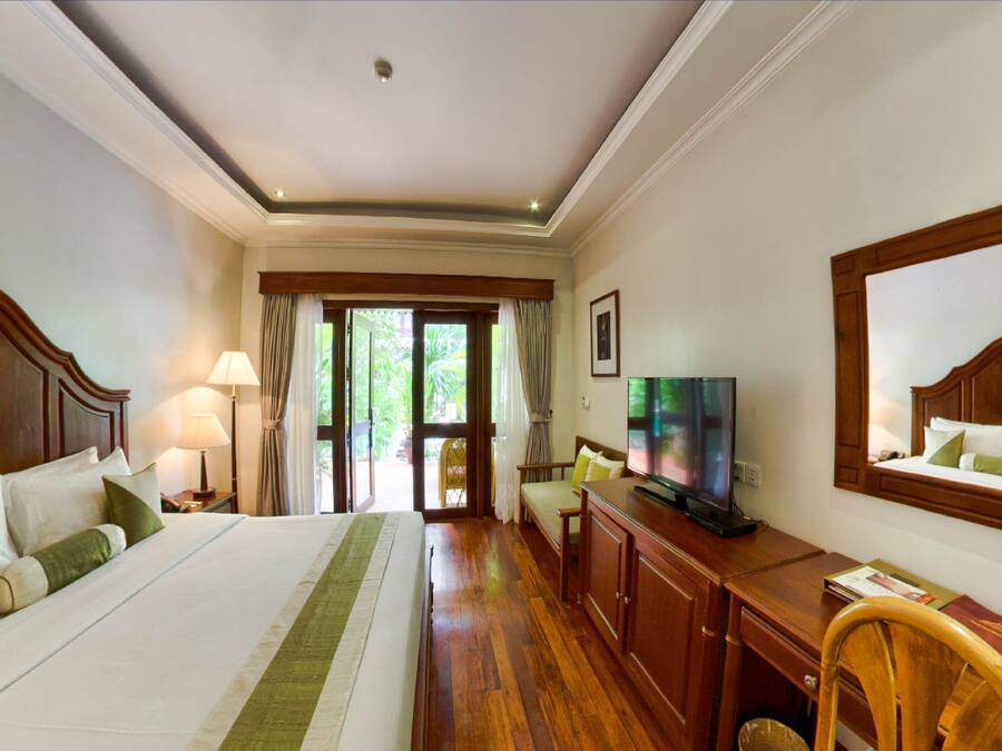 A hotel room with a large bed, a desk with a TV, a chair, and a window with curtains.