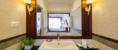A hotel bathroom with a large mirror, a white sink, and two wall-mounted lamps.