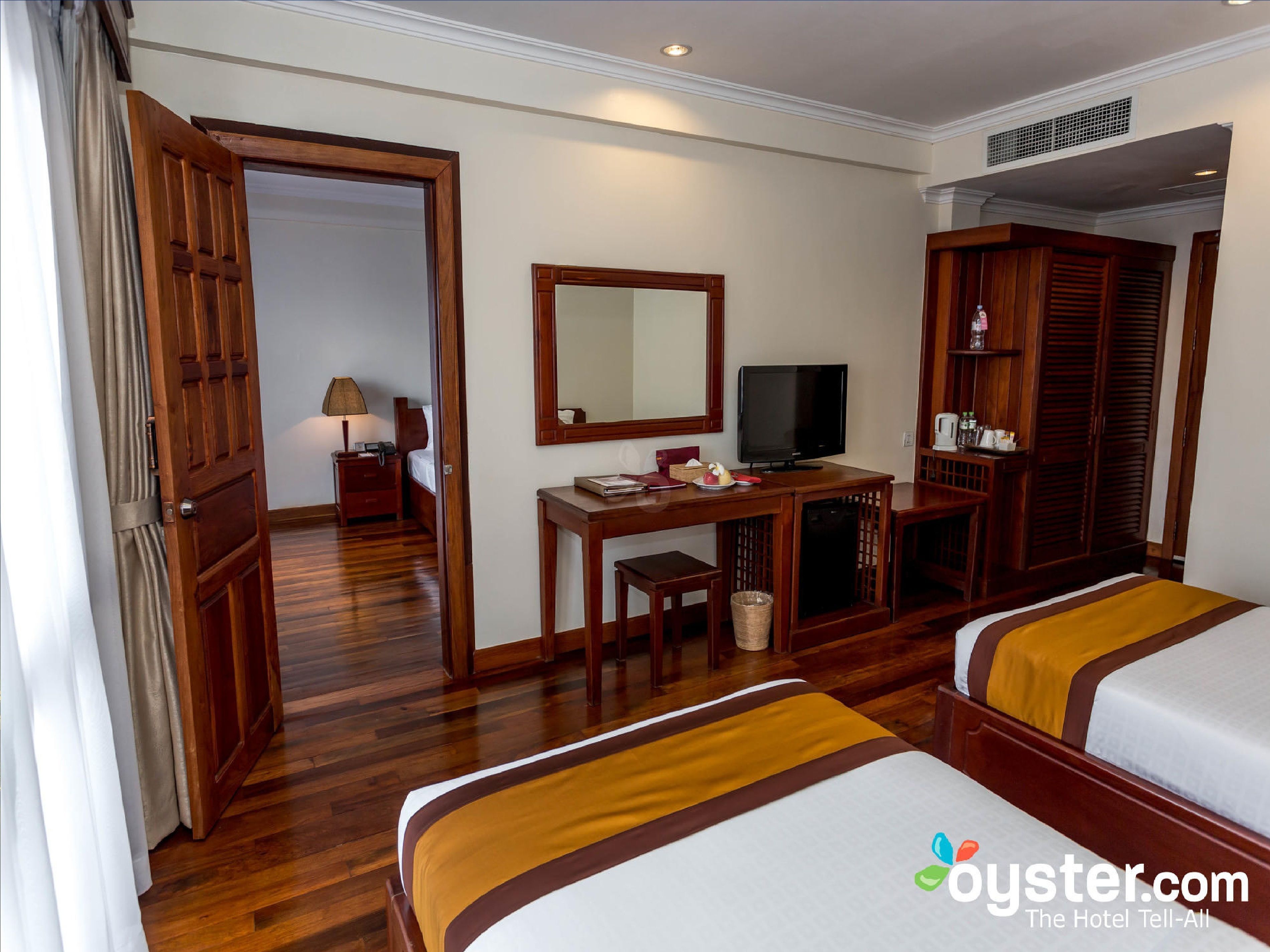 Una habitación de hotel con dos camas, un escritorio con televisor, un armario y un espejo.