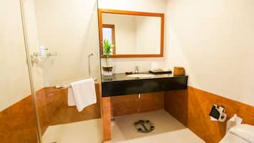 A bathroom with a glass shower enclosure, a black sink, a mirror with a wooden frame, a toilet, and a small potted plant.