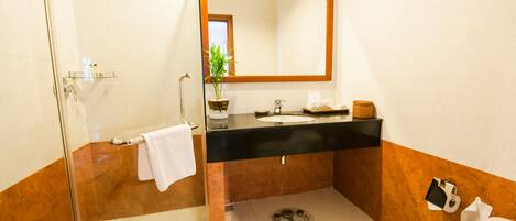 A bathroom with a glass shower enclosure, a black sink, a mirror with a wooden frame, a toilet, and a small potted plant.