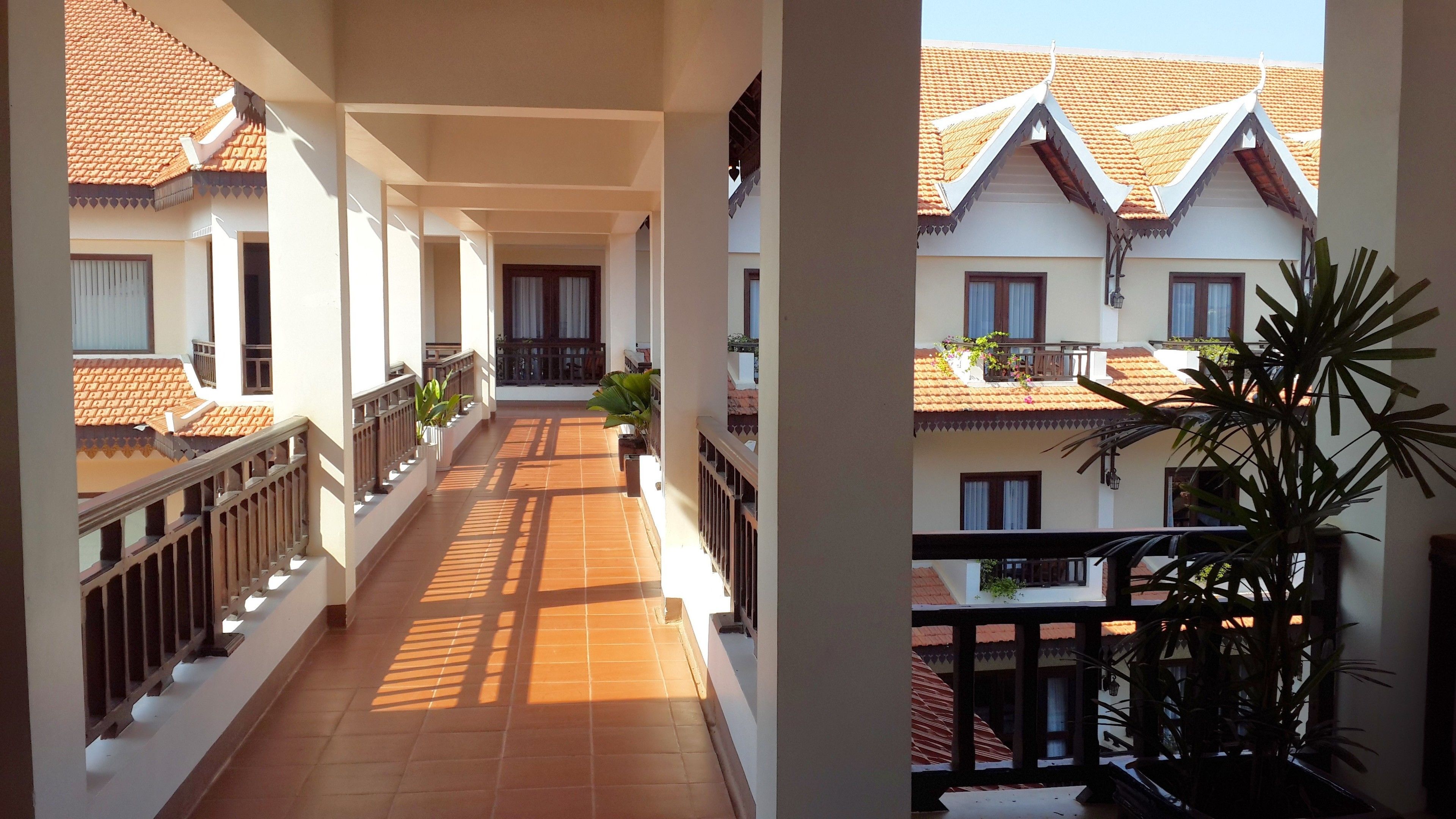 A corridor with tiled flooring, white walls, and balconies with railings.
