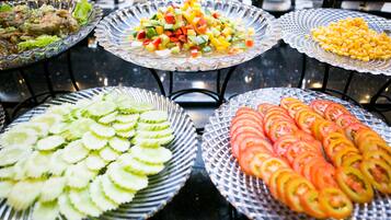 Un buffet proposant divers plats, notamment des concombres et des tomates en tranches, ainsi qu’une salade de fruits colorée.