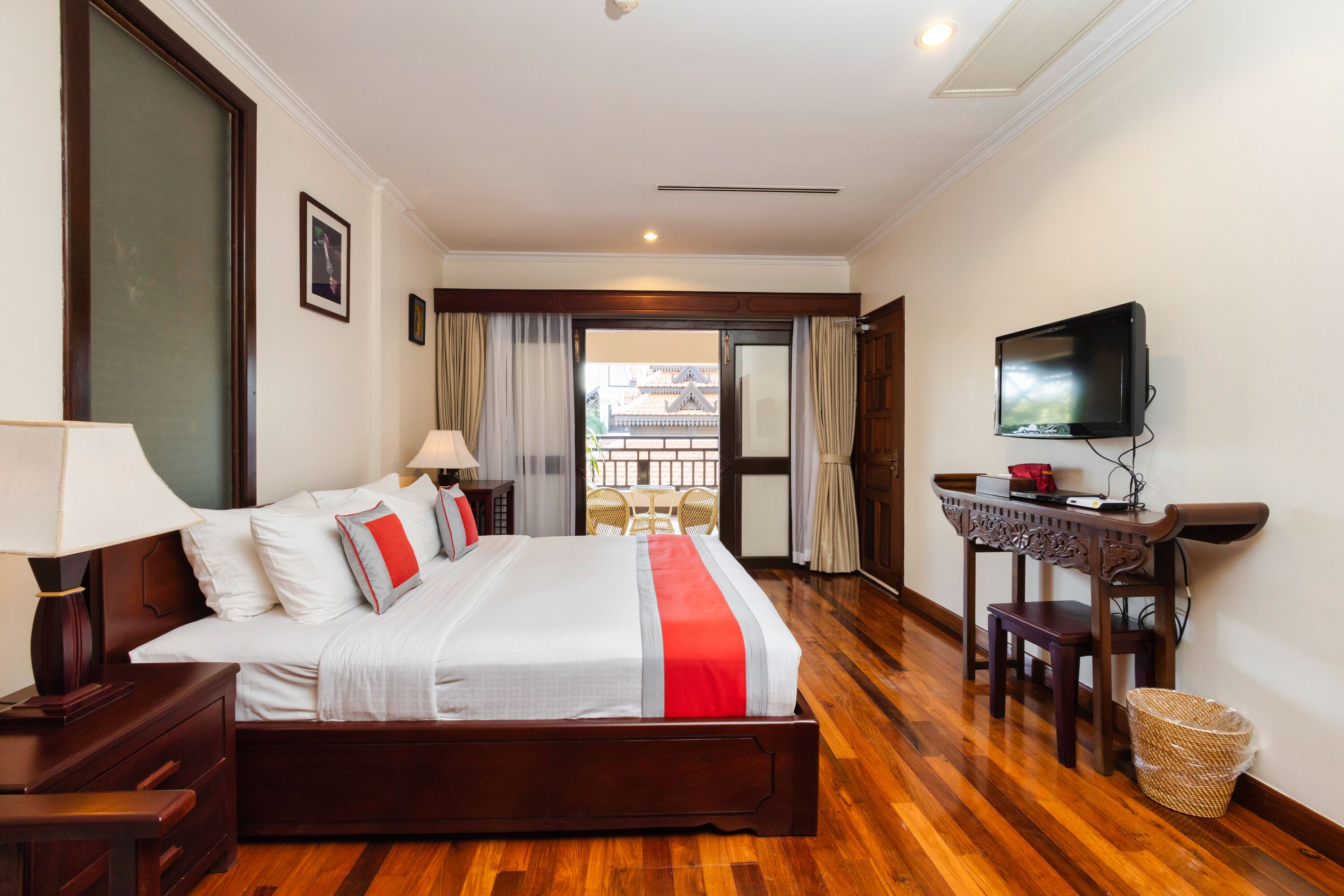 Quarto de hotel com uma cama grande, televisão, escrivaninha com cadeira e vista para um edifício tradicional pela porta.