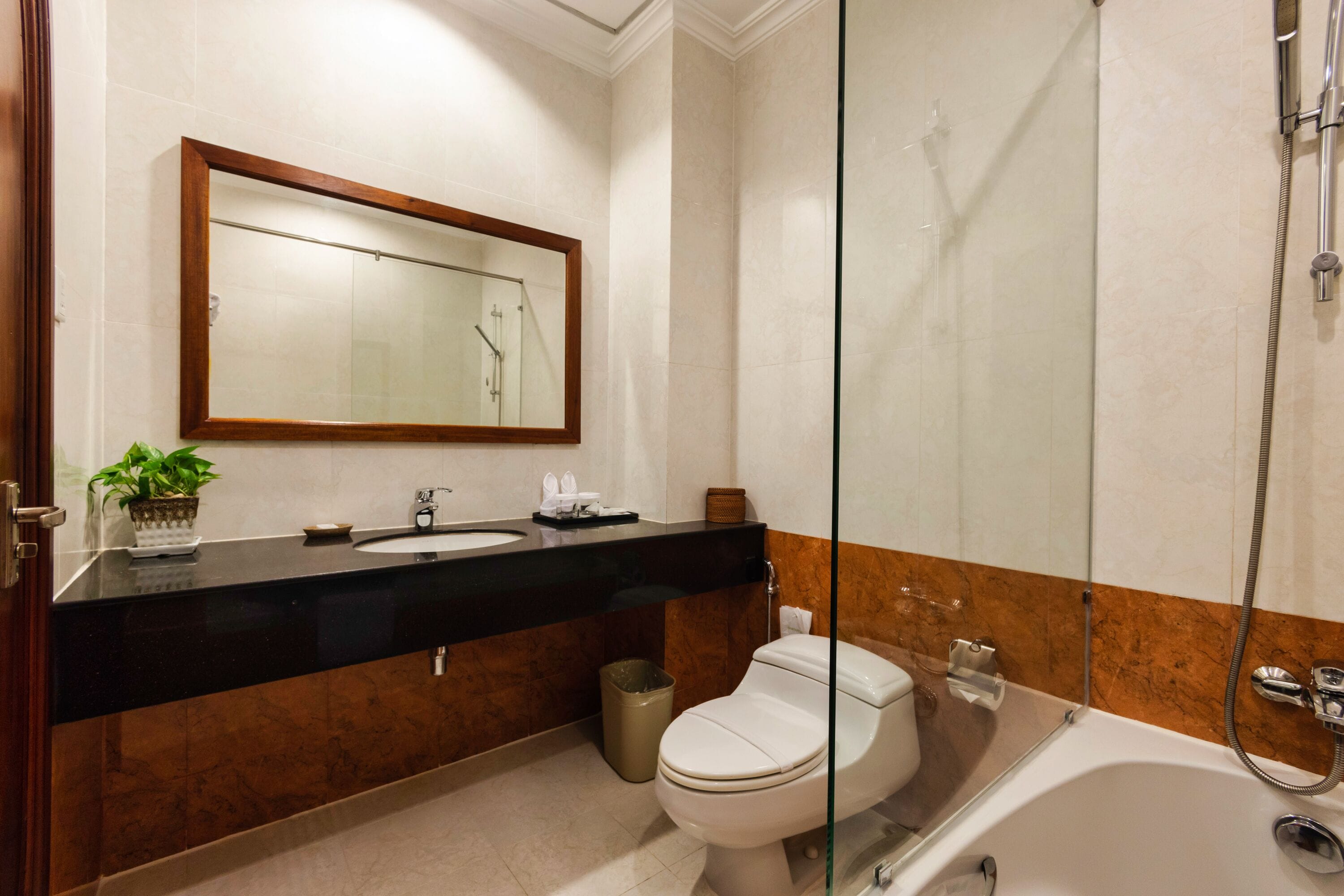 A modern bathroom with a black countertop, a white toilet, a glass-enclosed shower, and a large mirror above the sink.