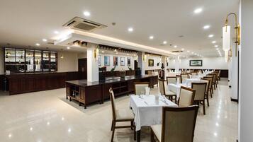 A spacious restaurant with multiple dining tables and chairs, a bar area, and a well-lit ceiling with recessed lighting.