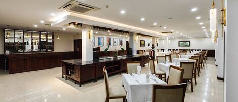 A spacious restaurant with multiple dining tables and chairs, a bar area, and a well-lit ceiling with recessed lighting.