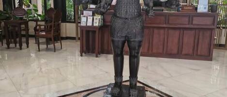 Una estatua en un vestíbulo con piso de baldosas y una recepción al fondo.