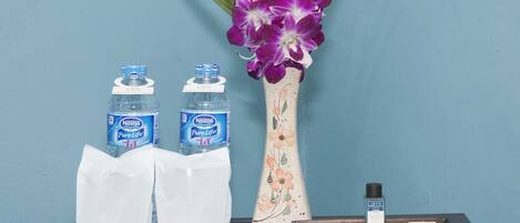 Un minibar con dos botellas de agua Nestlé Pure Life, un florero con flores moradas y una bandeja con una pastilla de jabón y una botella de loción.