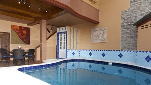 An indoor swimming pool with blue and white tiles, a staircase, and a dining area with chairs.