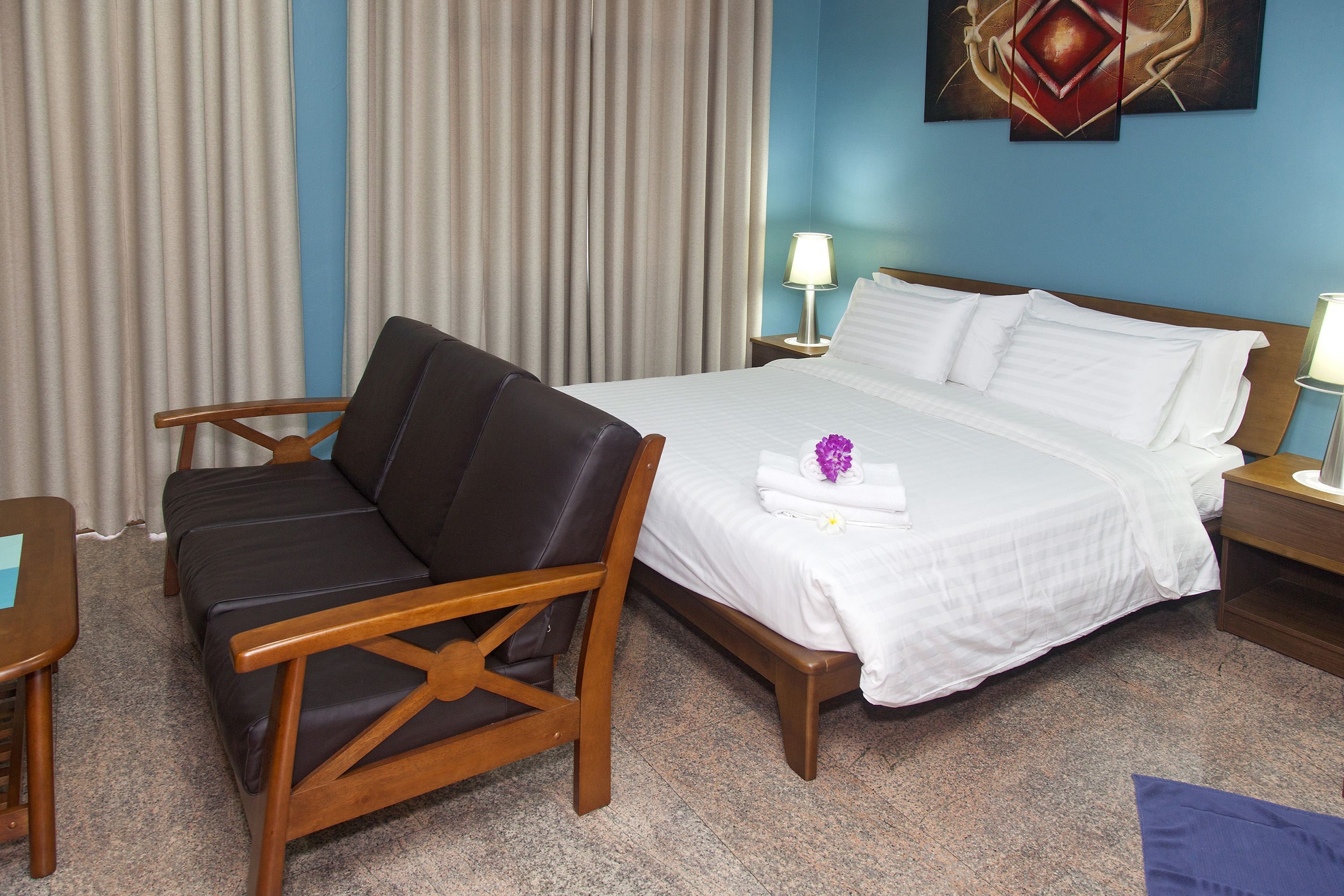 Una habitación de hotel con una cama, una silla de madera, una mesita de noche y una lámpara.