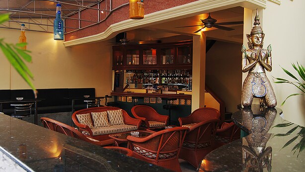 A bar area with wicker furniture, a Buddha statue, and a well-stocked bar.