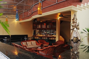 Un área de bar con mobiliario de mimbre, una estatua de Buda y una barra bien surtida.