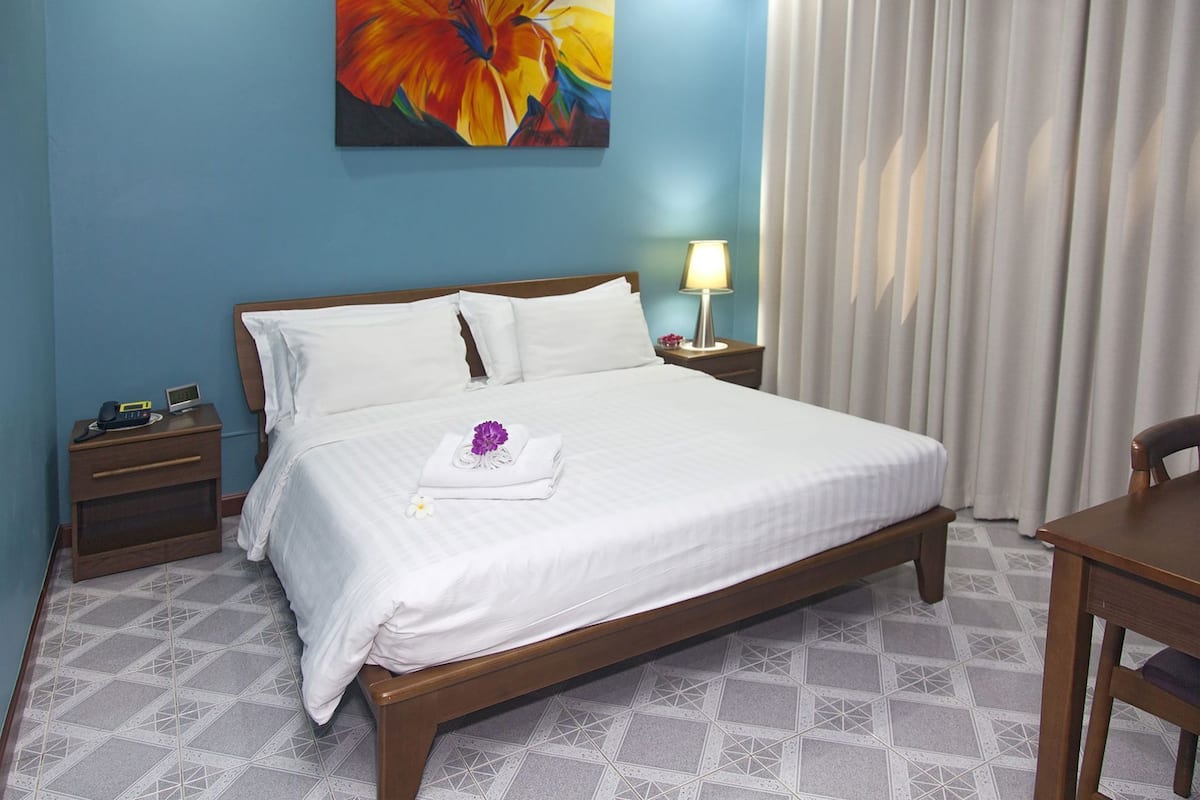 Une chambre d’hôtel avec un lit, une table de chevet, un bureau, une lampe et un tableau au mur.