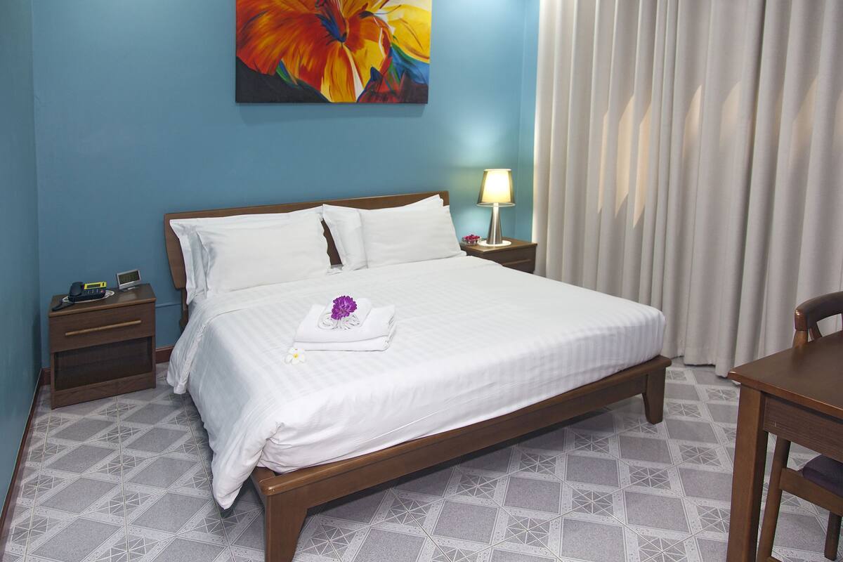 Une chambre d’hôtel avec un grand lit, une table de chevet avec une lampe, une chaise en bois et un tableau au mur.