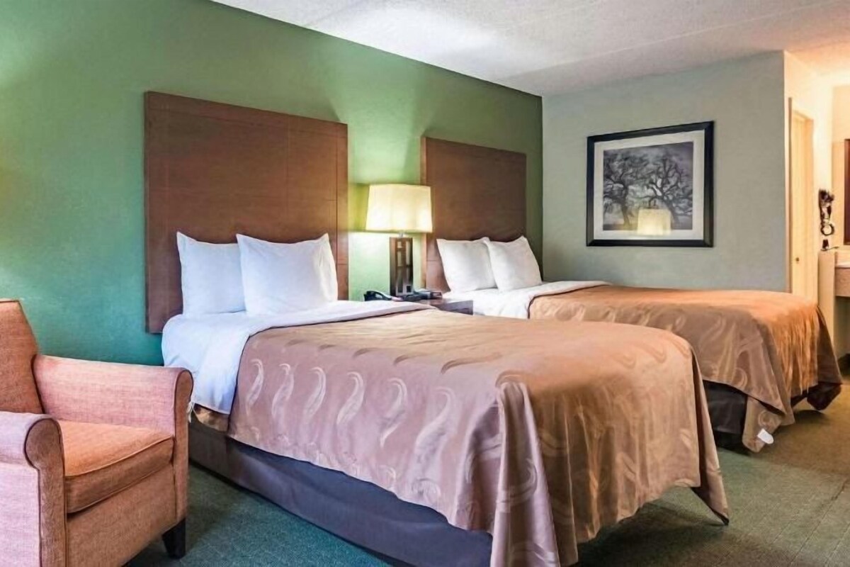 Quarto de hotel com duas camas, uma cadeira e luminárias.