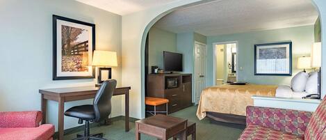 A hotel room with a desk, chair, sofa, and a bed with a beige cover.