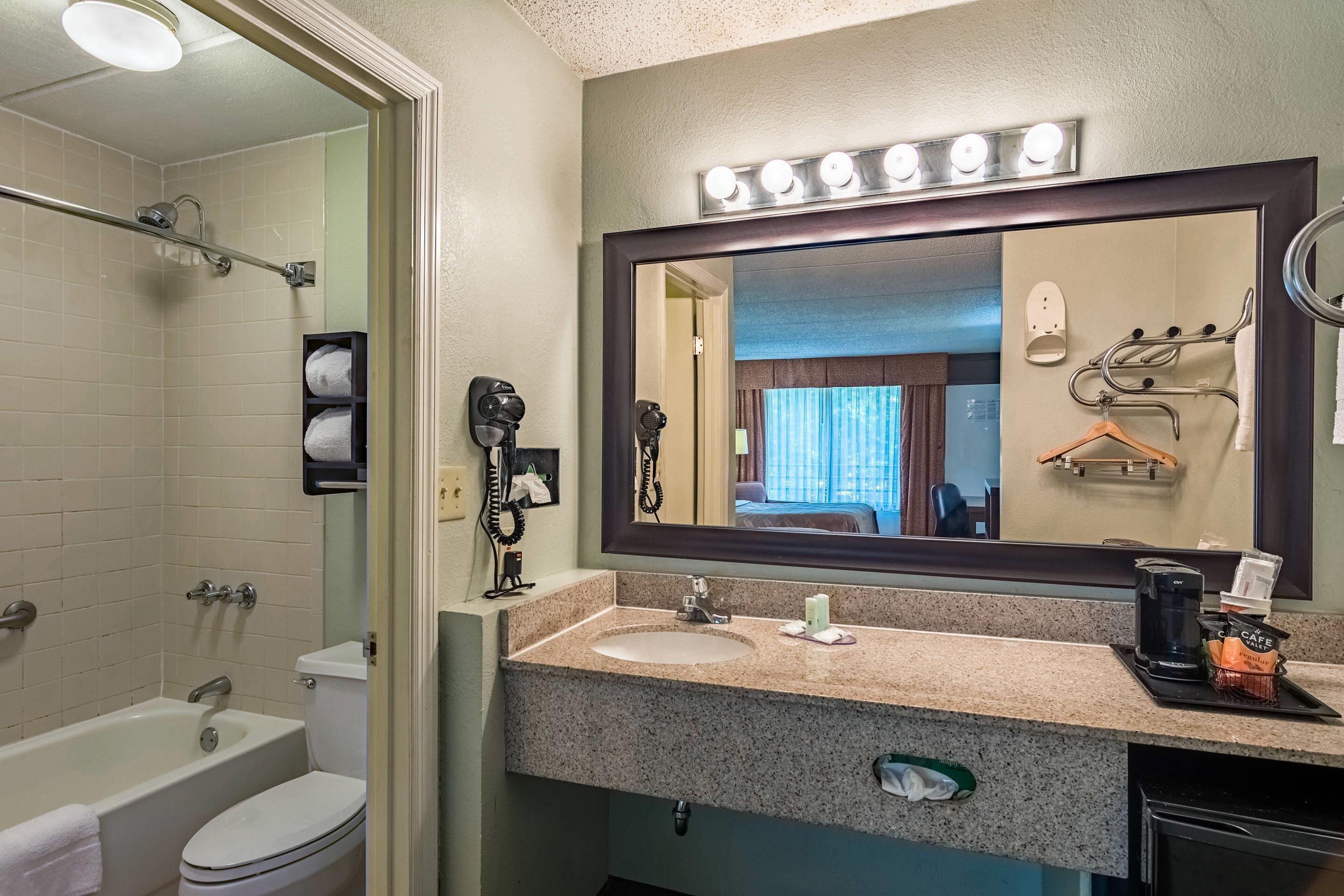 A hotel bathroom with a sink, mirror, towel rack, and a shower area.