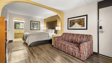 A hotel room with a bed, a sofa, a framed picture, and a door.
