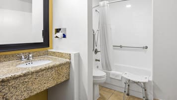 Une salle de bain avec un lavabo sur un plan de toilette en granit, des toilettes et une douche équipée d’une barre d’appui.