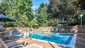 A swimming pool with lounge chairs and umbrellas, surrounded by a wooden fence and trees.