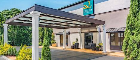 A covered outdoor area with a canopy, a building with a 'Quality Inn' sign, and potted plants.