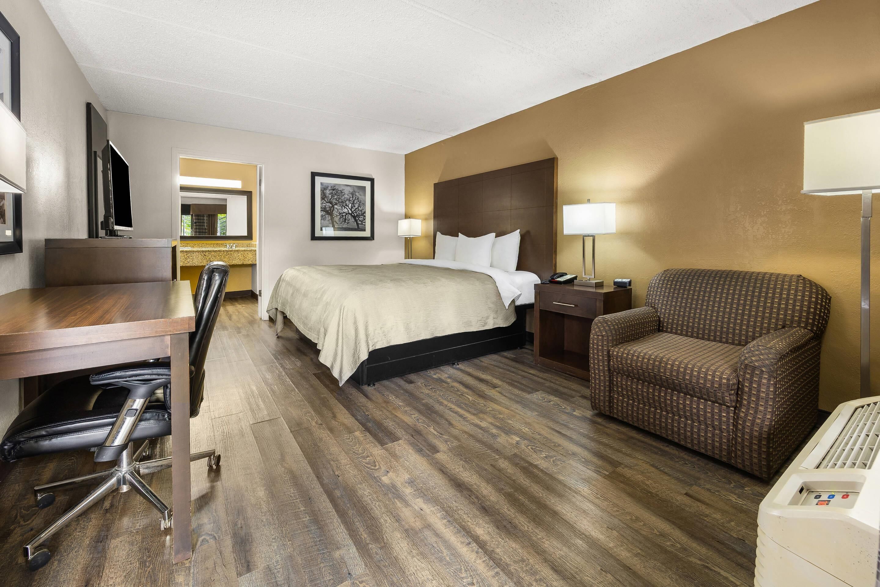 Habitación de hotel con cama, escritorio, silla y una mesita de noche con lámpara.