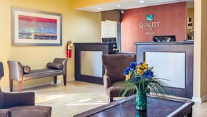 A reception area with a reception desk, two sofas, a framed painting, and a vase with flowers.