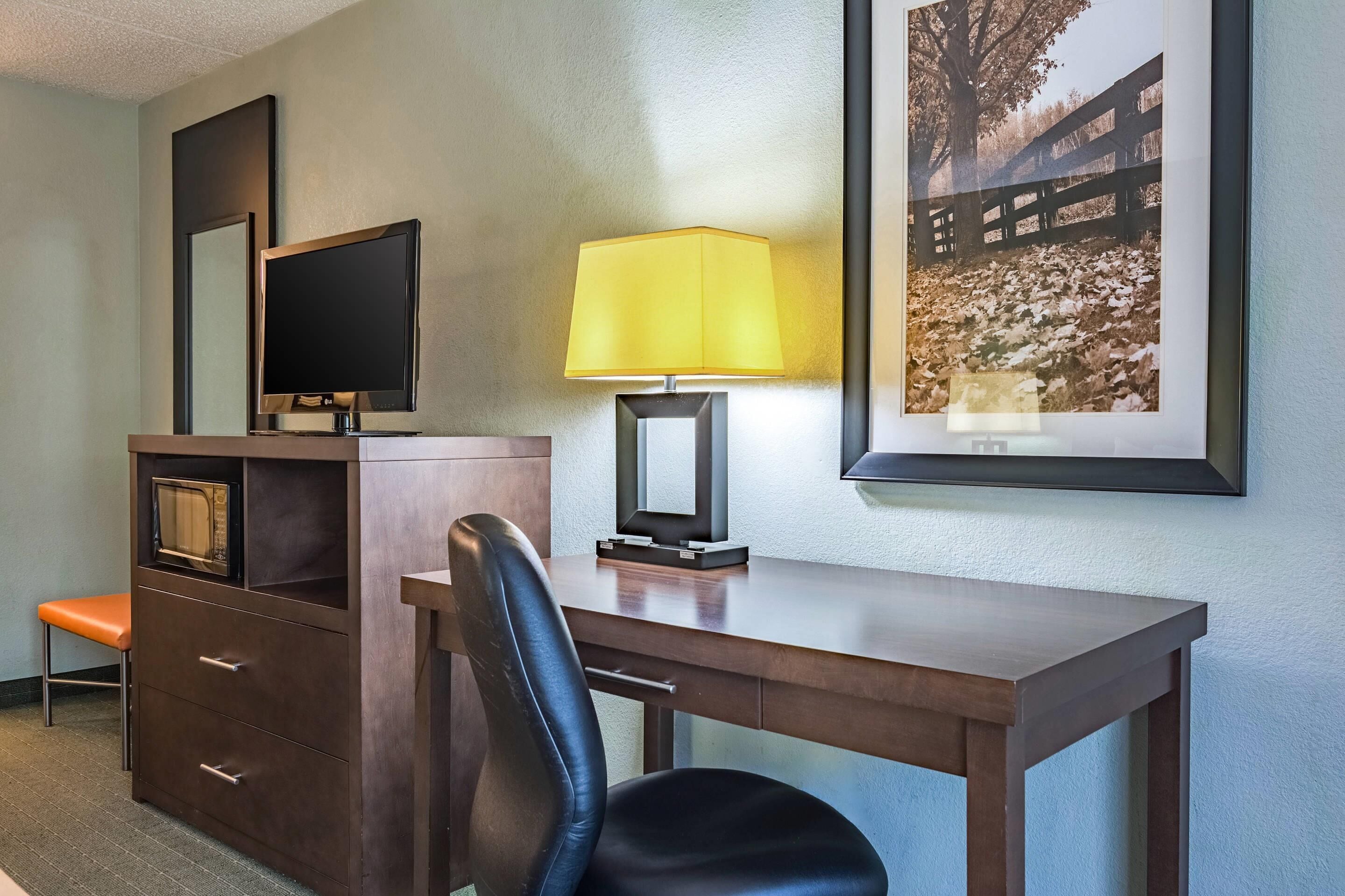 A hotel room with a desk, chair, television, lamp, and a framed picture on the wall.