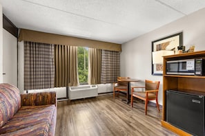 Hotellihuone, jossa on sohva, ruokapöytä tuoleineen, mikroaaltouuni ja pieni jääkaappi.
