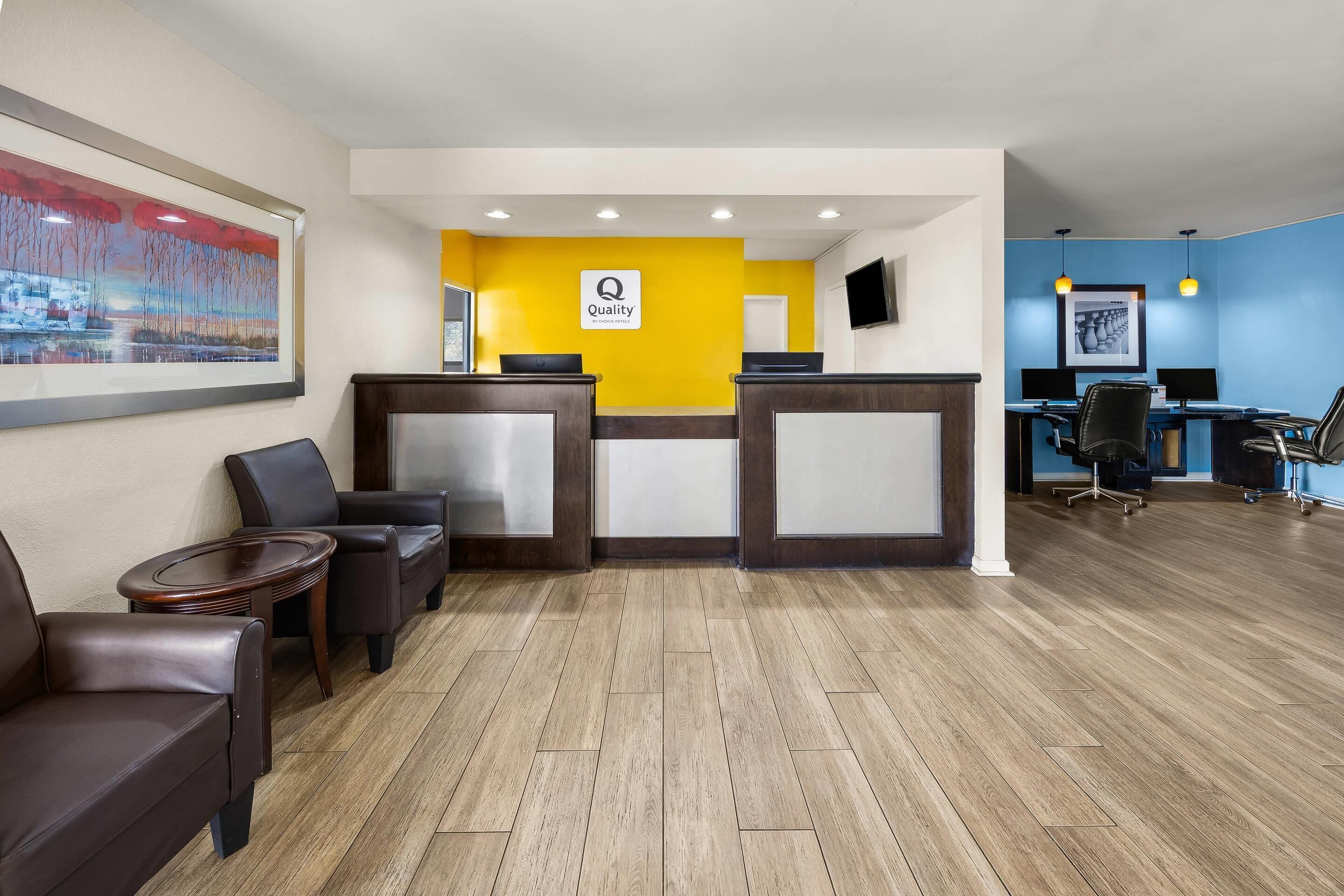 A hotel reception area with a desk, chairs, and a painting on the wall.