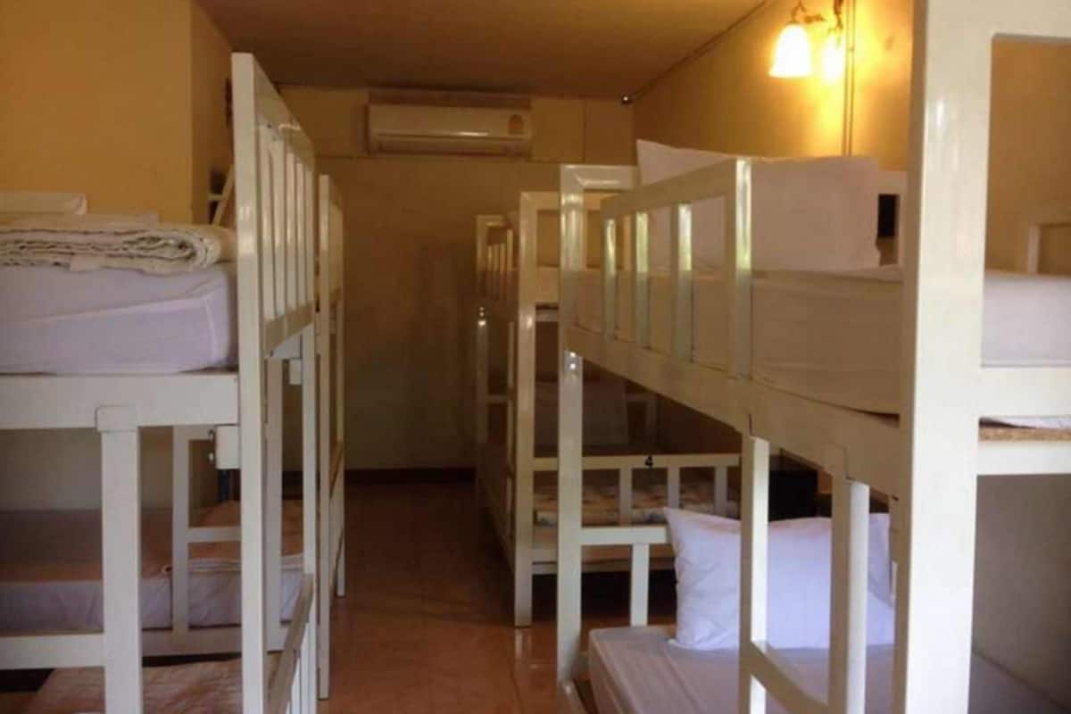 Un couloir étroit, avec des lits superposés de chaque côté, un climatiseur fixé au mur et un luminaire au-dessus des lits.