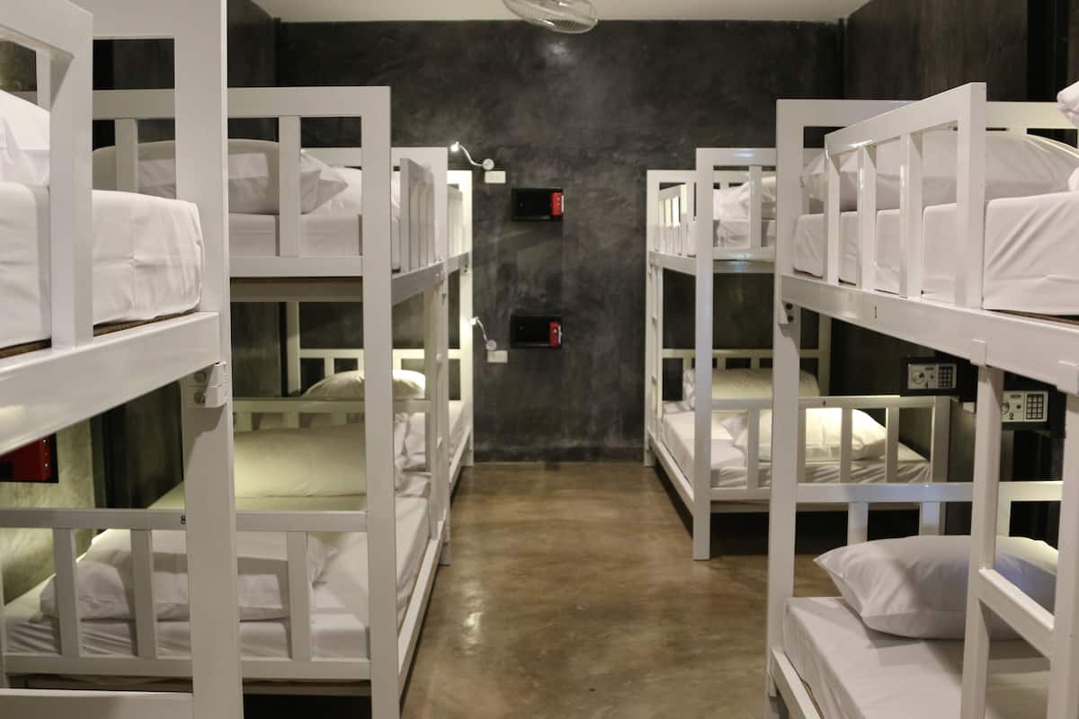 Une chambre avec des lits superposés blancs disposés en deux rangées, un mur sombre et un sol en béton.