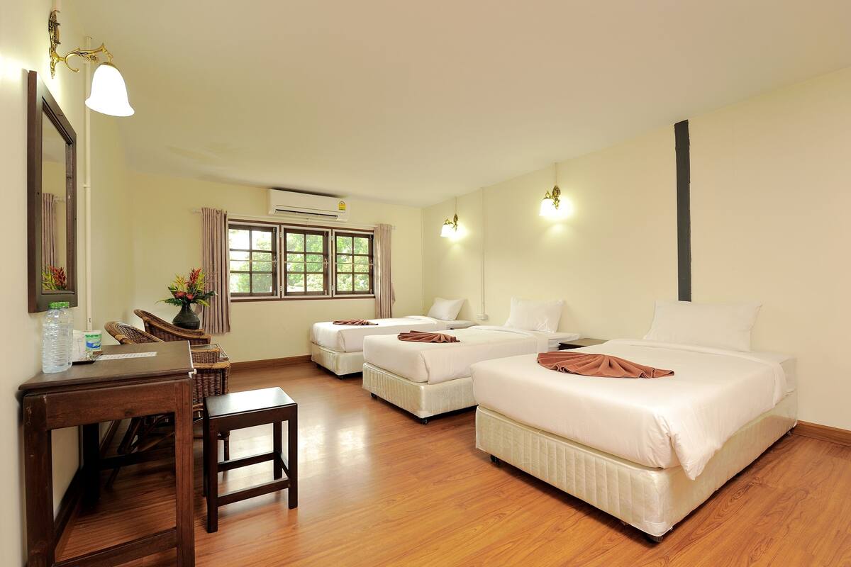 Une chambre d’hôtel avec deux lits simples, un bureau avec une chaise, une petite table et une fenêtre avec des rideaux.