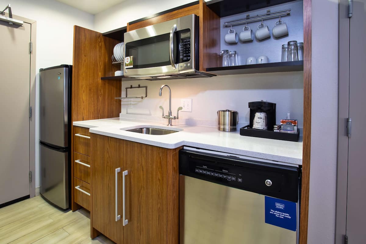A compact kitchen with a stainless steel refrigerator, a microwave, a coffee maker, and a dishwasher.