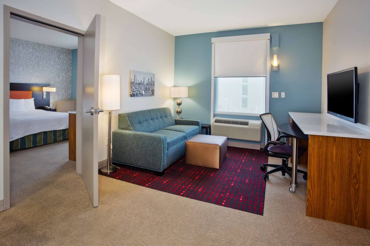 A hotel room with a bed, a sofa, a desk, and a TV.