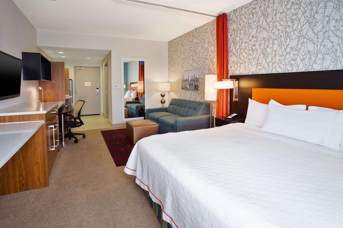 A hotel room with a large bed, a desk, a chair, a sofa, and a TV.