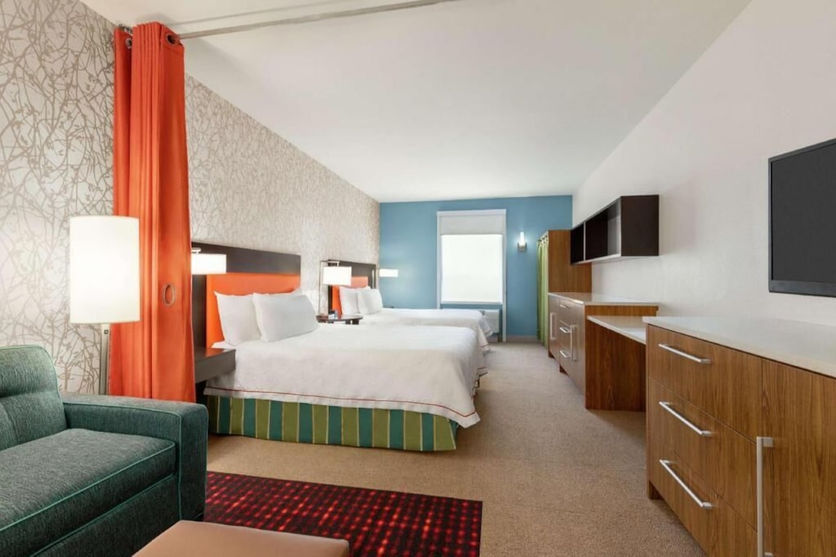 Een hotelkamer met twee bedden, een bank, een televisie, een bureau en een raam.