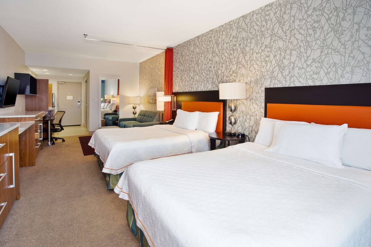A hotel room with two beds, a desk, a chair, and a TV.