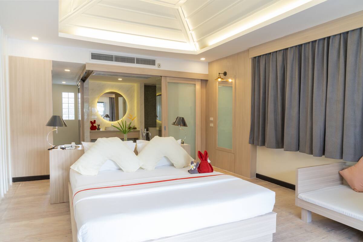 A modern hotel room with a neatly made bed, a sitting area, and a large window with curtains.